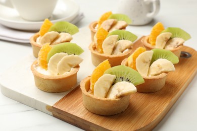 Photo of Tartlets with fruits on white marble table, closeup. Delicious dessert