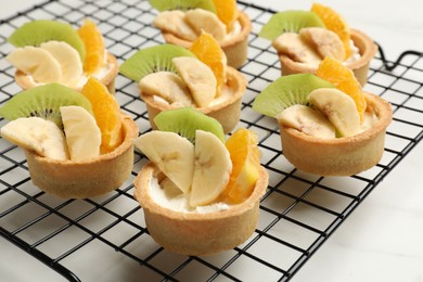 Photo of Tartlets with fruits on white marble table, closeup. Delicious dessert