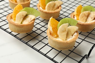 Photo of Tartlets with fruits on white marble table, closeup. Delicious dessert