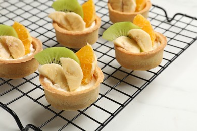 Photo of Tartlets with fruits on white marble table, closeup. Delicious dessert