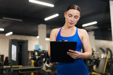 Photo of Professional personal trainer with clipboard in gym. Space for text