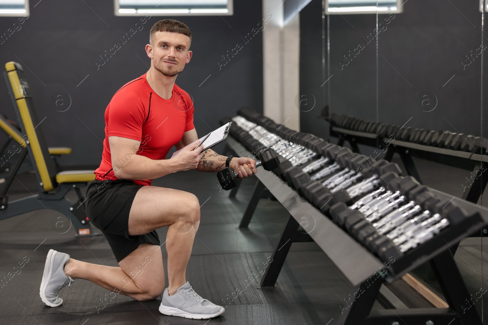 Personal trainer with clipboard and dumbbells in gym Photo of Personal trainer with clipboard and dumbbells in gym