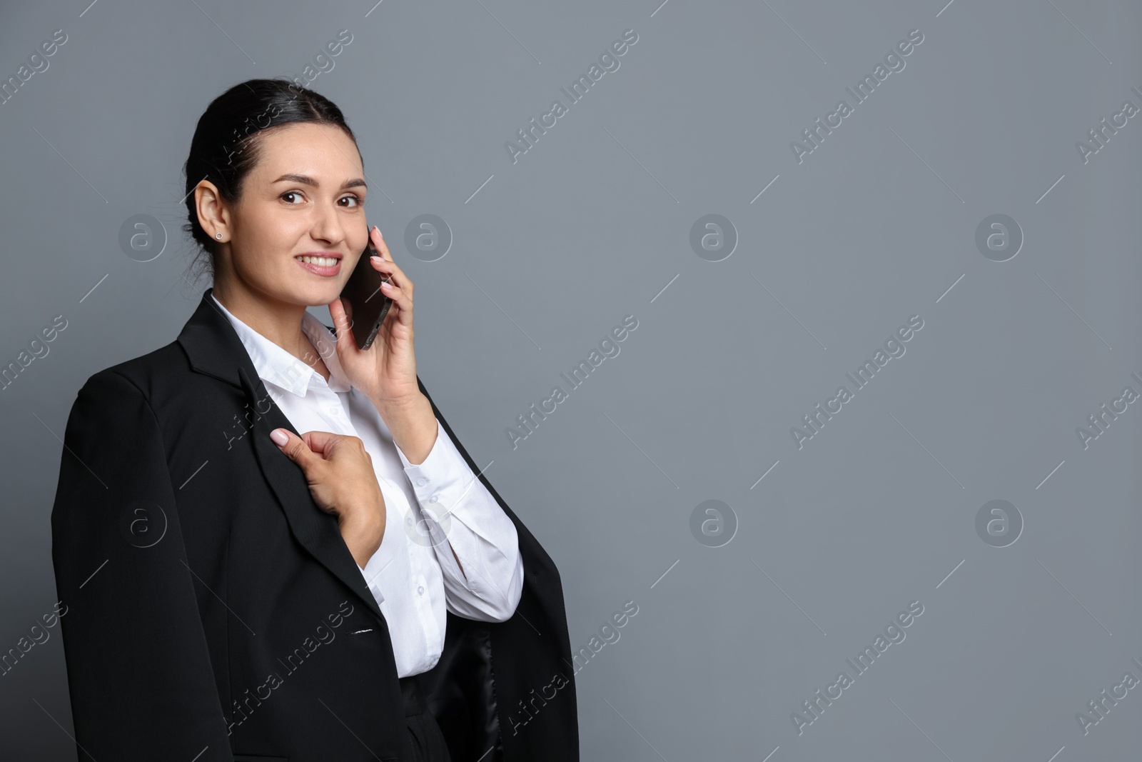 Confident business woman in suit talking on phone against grey background. Space for text Photo of Confident business woman in suit talking on phone against grey background. Space for text