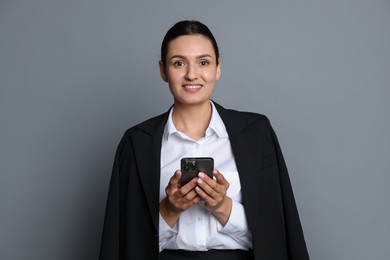 Photo of Confident business woman in suit with smartphone on grey background