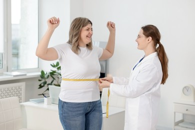 Photo of Weight loss. Nutritionist measuring happy overweight woman's waist with tape in clinic