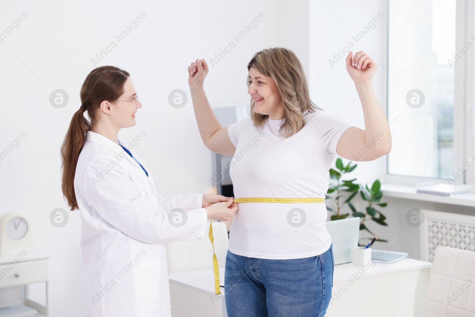 Weight loss. Nutritionist measuring happy overweight woman's waist with tape in clinic Photo of Weight loss. Nutritionist measuring happy overweight woman's waist with tape in clinic
