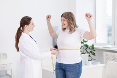 Photo of Weight loss. Nutritionist measuring happy overweight woman's waist with tape in clinic