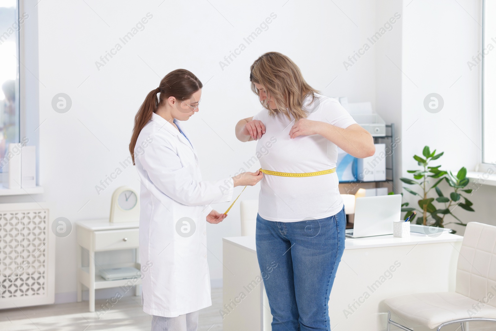 Photo of Weight loss. Nutritionist measuring overweight woman's waist with tape in clinic
