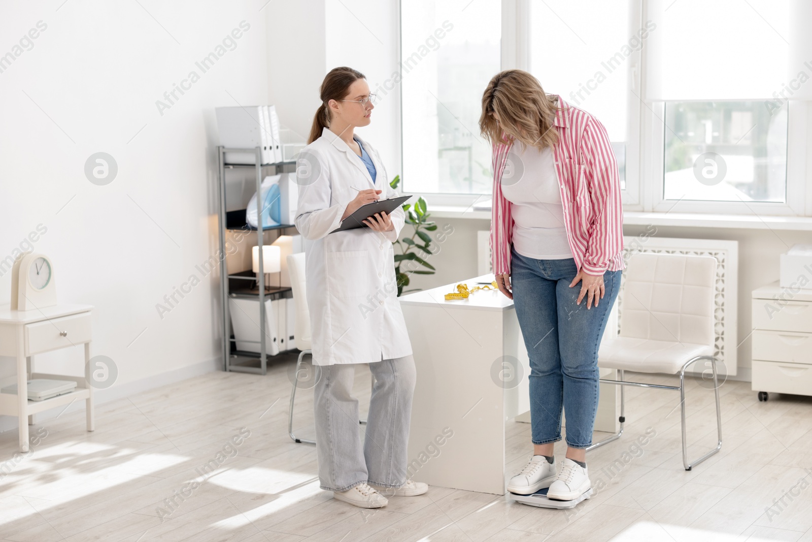 Weight loss. Overweight woman standing on scales during consultation with nutritionist in clinic Photo of Weight loss. Overweight woman standing on scales during consultation with nutritionist in clinic