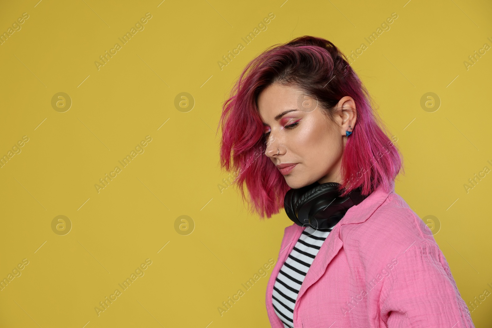 Beautiful woman with pink dyed hair and headphones on yellow background, space for text Photo of Beautiful woman with pink dyed hair and headphones on yellow background, space for text