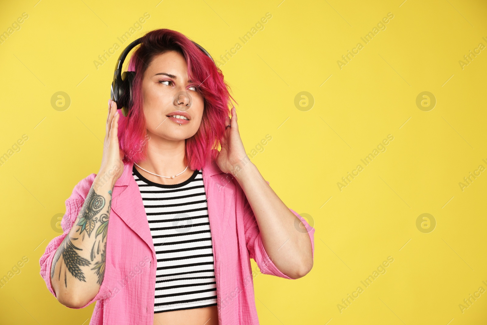 Beautiful woman with pink dyed hair listening to music on yellow background, space for text Photo of Beautiful woman with pink dyed hair listening to music on yellow background, space for text
