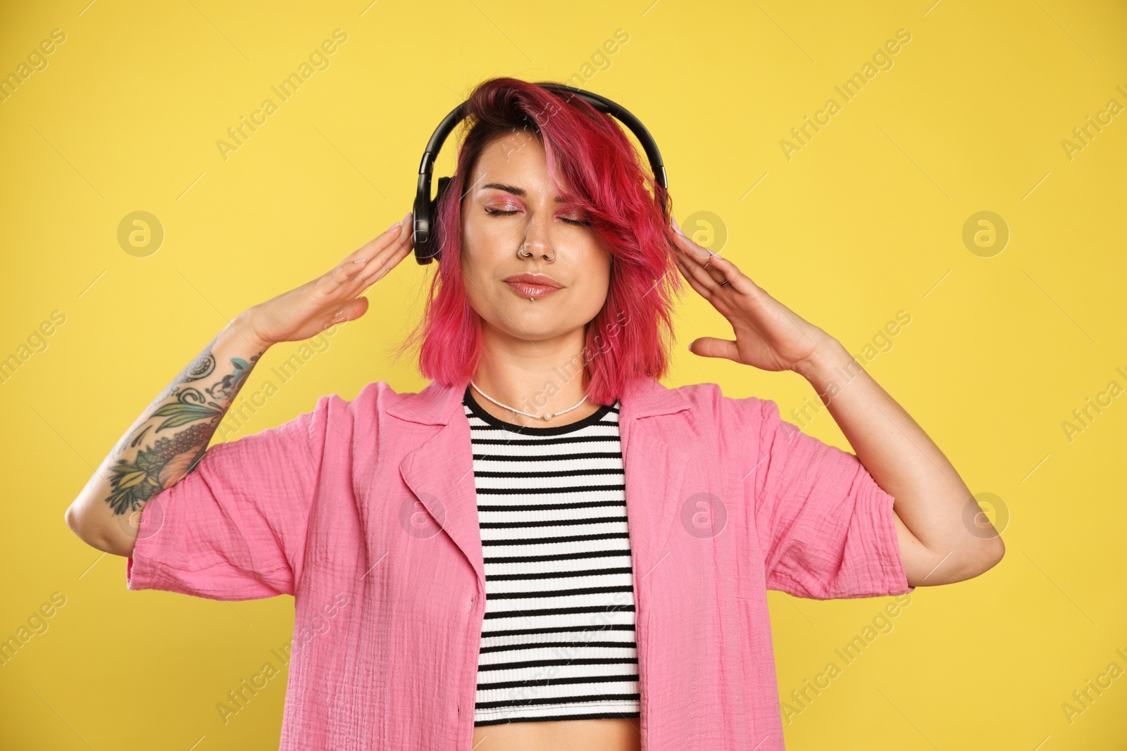 Beautiful woman with pink dyed hair listening to music on yellow background Photo of Beautiful woman with pink dyed hair listening to music on yellow background
