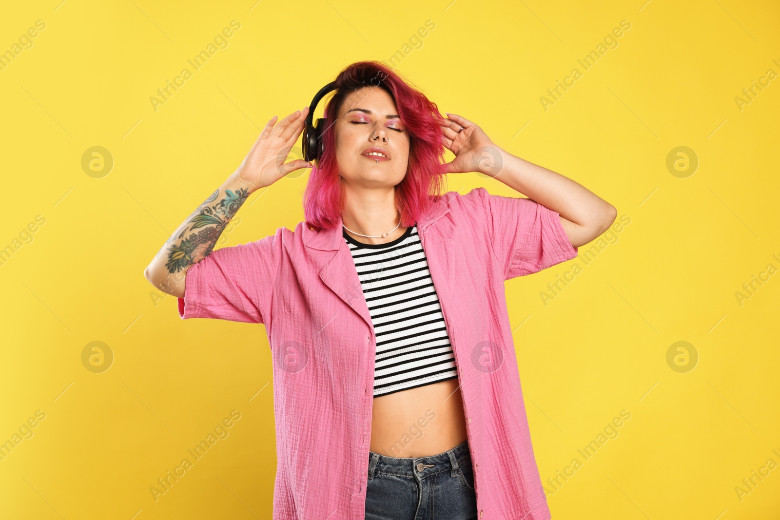 Beautiful woman with pink dyed hair listening to music on yellow background Photo of Beautiful woman with pink dyed hair listening to music on yellow background