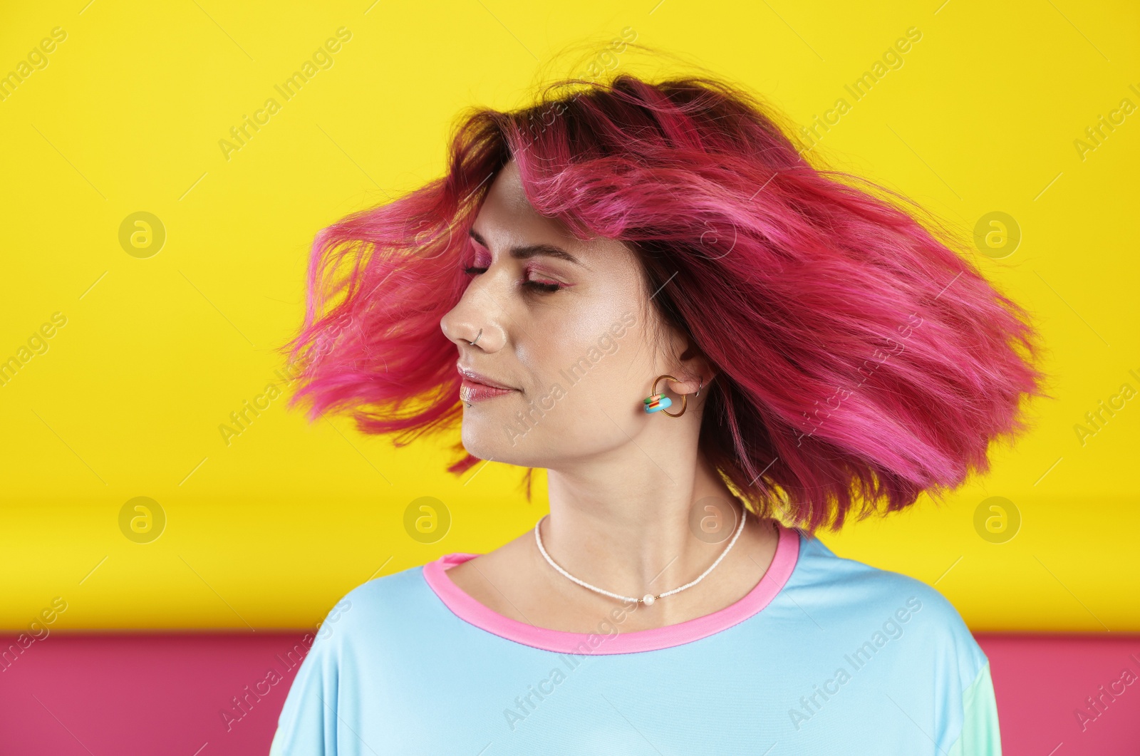 Beautiful woman with pink dyed hair shaking head on color background Photo of Beautiful woman with pink dyed hair shaking head on color background
