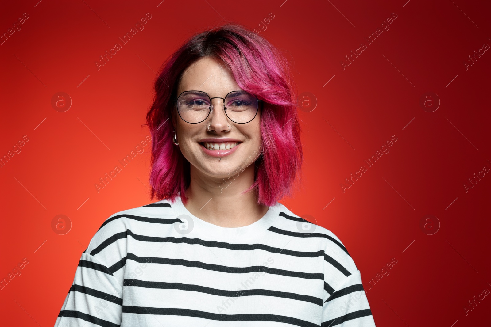 Beautiful woman with pink dyed hair in glasses on red gradient background Photo of Beautiful woman with pink dyed hair in glasses on red gradient background
