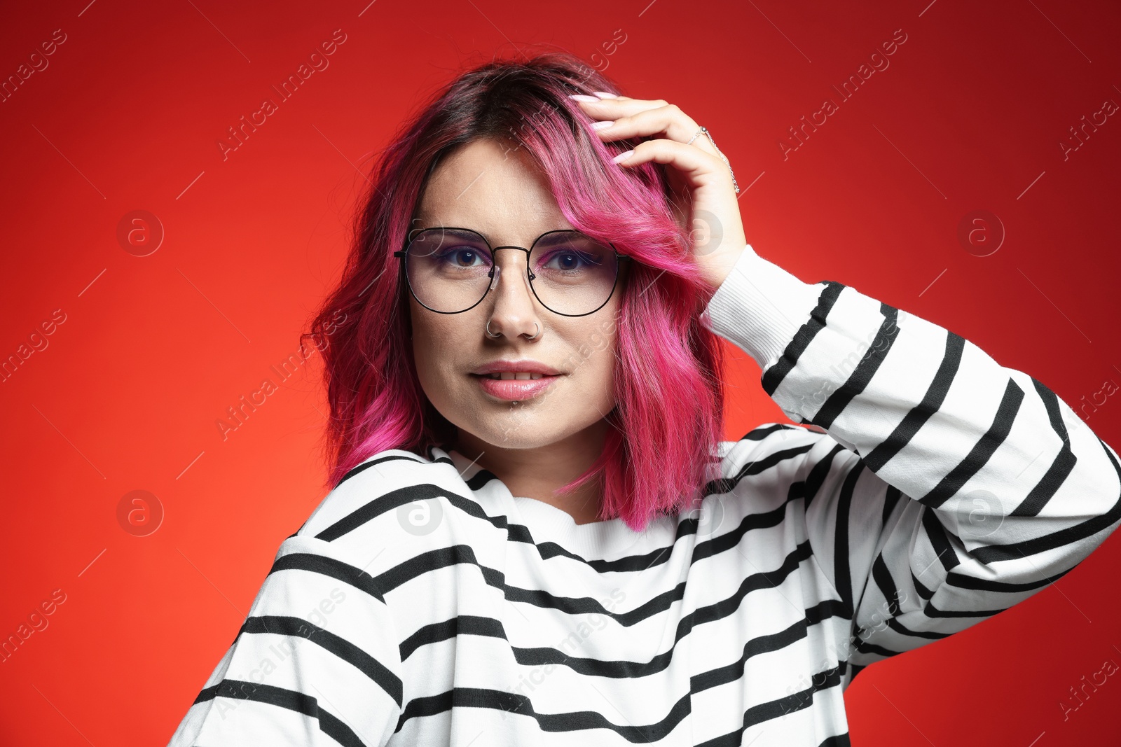 Beautiful woman with pink dyed hair in glasses on red gradient background Photo of Beautiful woman with pink dyed hair in glasses on red gradient background