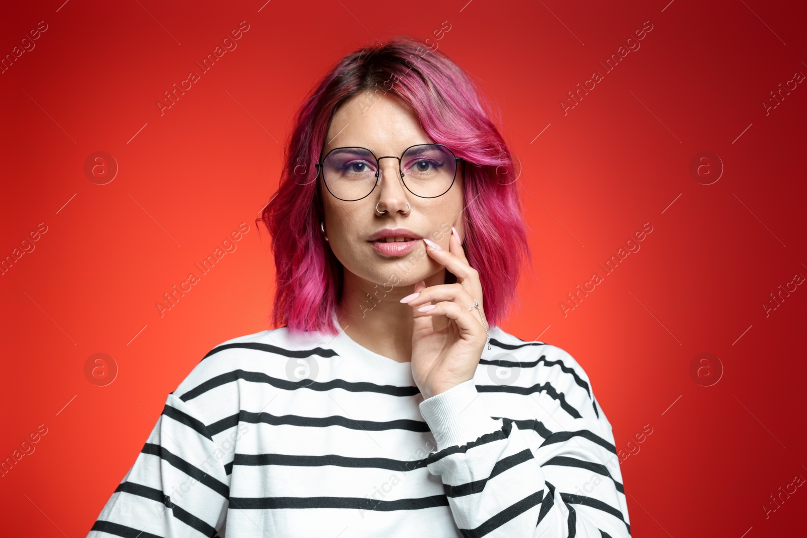 Beautiful woman with pink dyed hair in glasses on red gradient background Photo of Beautiful woman with pink dyed hair in glasses on red gradient background