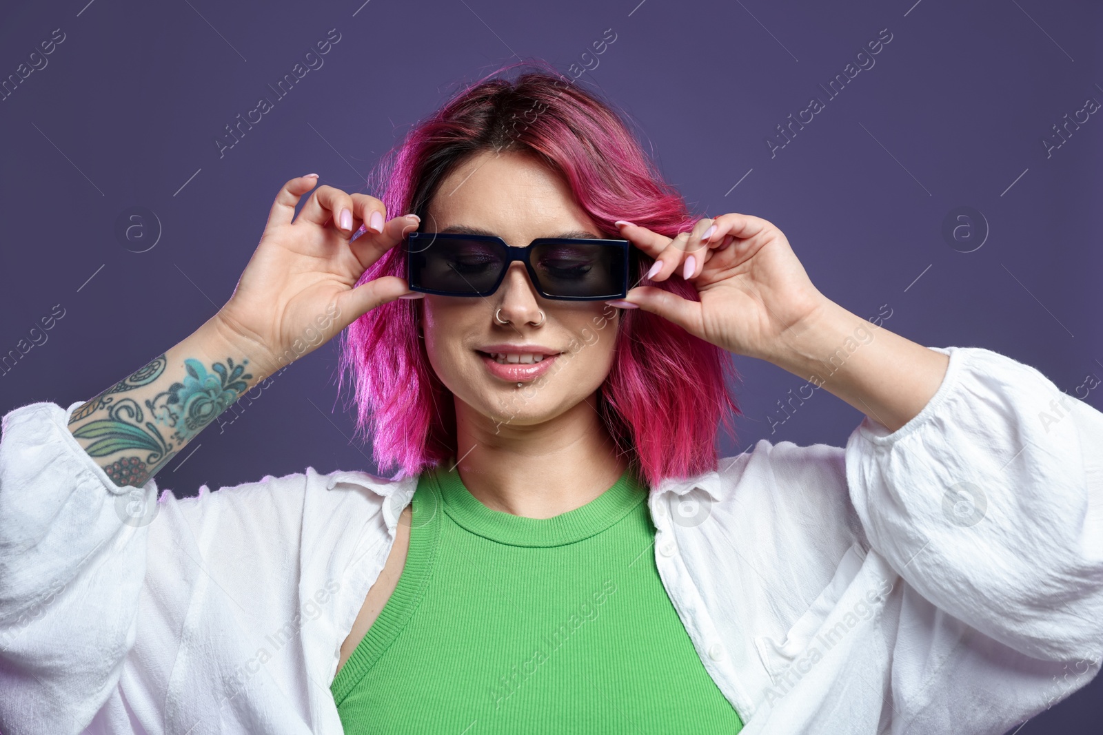 Beautiful woman with pink dyed hair in sunglasses on violet background Photo of Beautiful woman with pink dyed hair in sunglasses on violet background