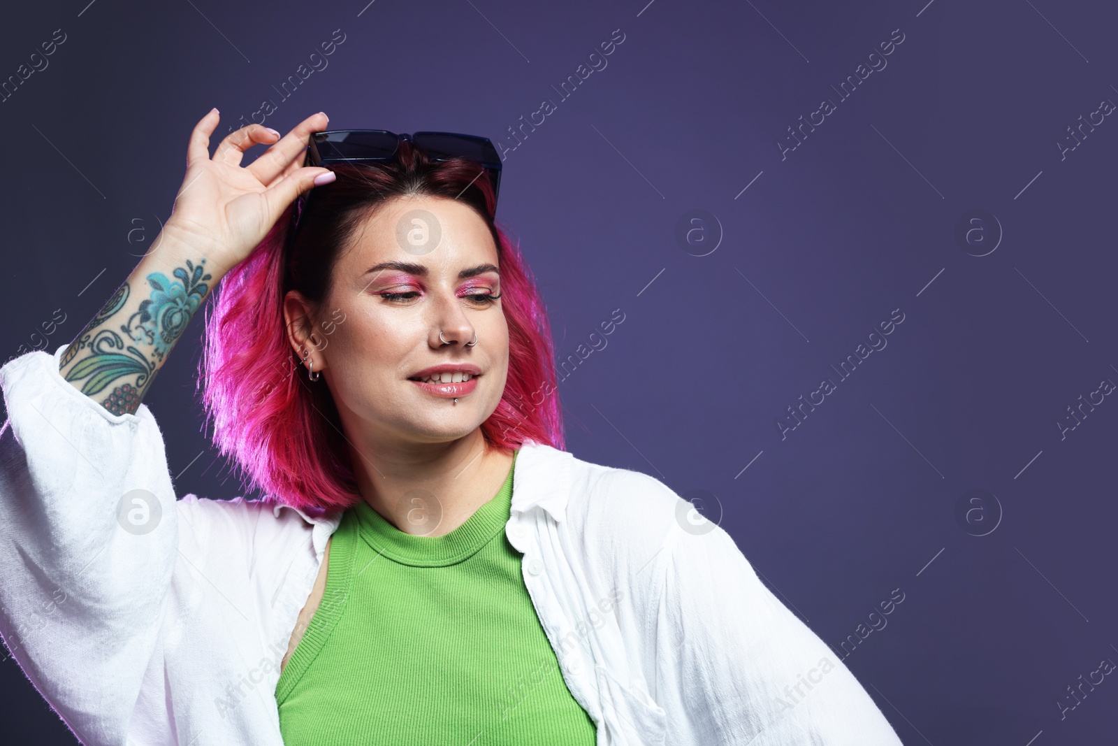 Beautiful woman with pink dyed hair in sunglasses on violet background, space for text Photo of Beautiful woman with pink dyed hair in sunglasses on violet background, space for text