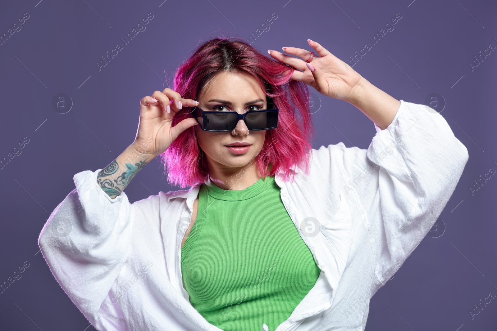Beautiful woman with pink dyed hair in sunglasses on violet background Photo of Beautiful woman with pink dyed hair in sunglasses on violet background