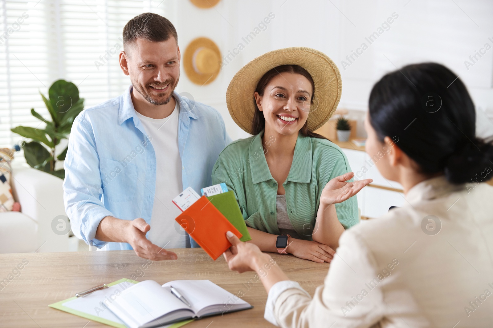 Happy couple planning vacation with travel agent at wooden table in office Photo of Happy couple planning vacation with travel agent at wooden table in office