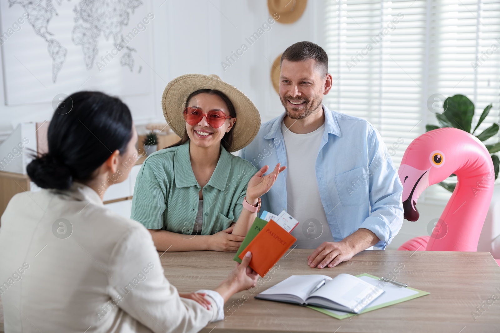 Happy couple planning vacation with travel agent at wooden table in office Photo of Happy couple planning vacation with travel agent at wooden table in office