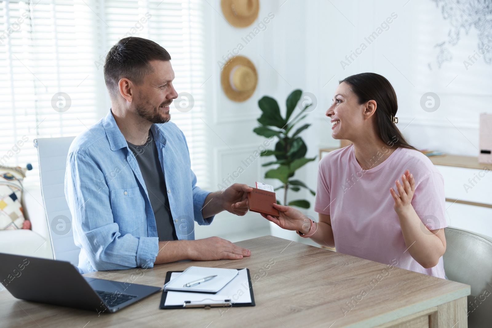 Travel agent giving passport with ticket to woman at wooden table in office Photo of Travel agent giving passport with ticket to woman at wooden table in office