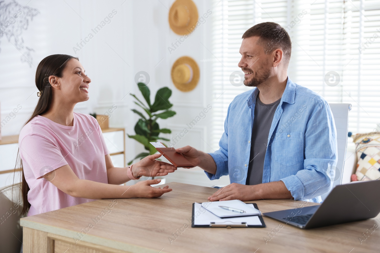 Travel agent giving passport with ticket to woman at wooden table in office Photo of Travel agent giving passport with ticket to woman at wooden table in office
