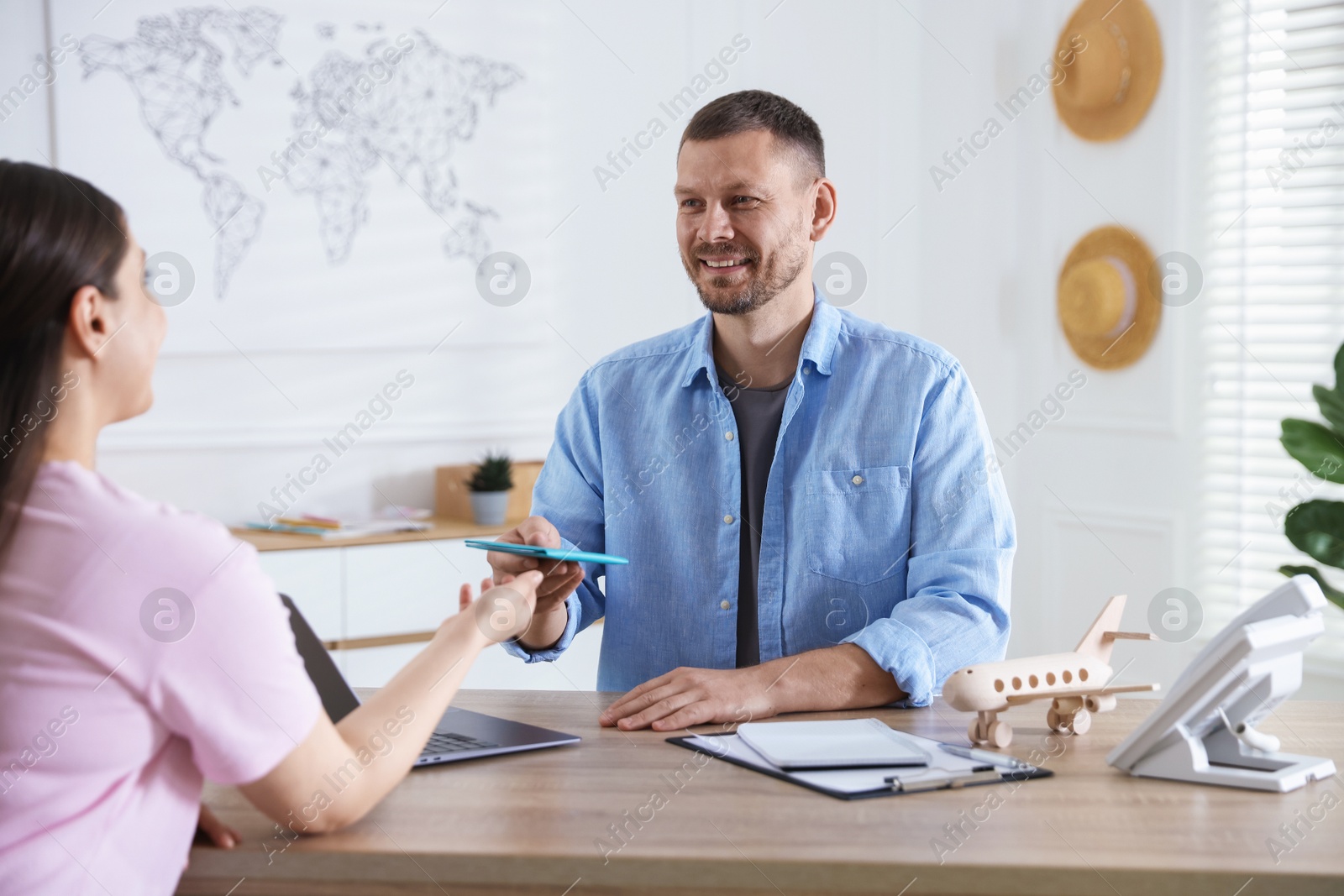Travel agent giving passport with ticket to woman at wooden table in office Photo of Travel agent giving passport with ticket to woman at wooden table in office