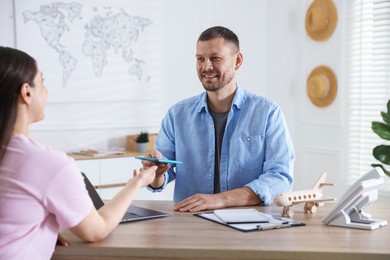 Photo of Travel agent giving passport with ticket to woman at wooden table in office