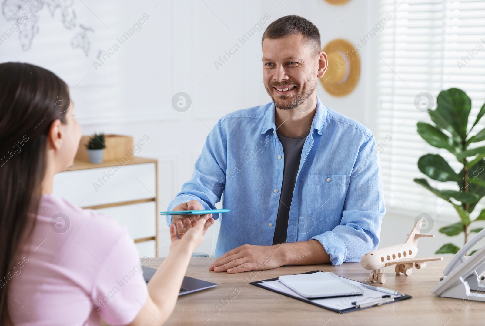 Travel agent giving passport with ticket to woman at wooden table in office Photo of Travel agent giving passport with ticket to woman at wooden table in office