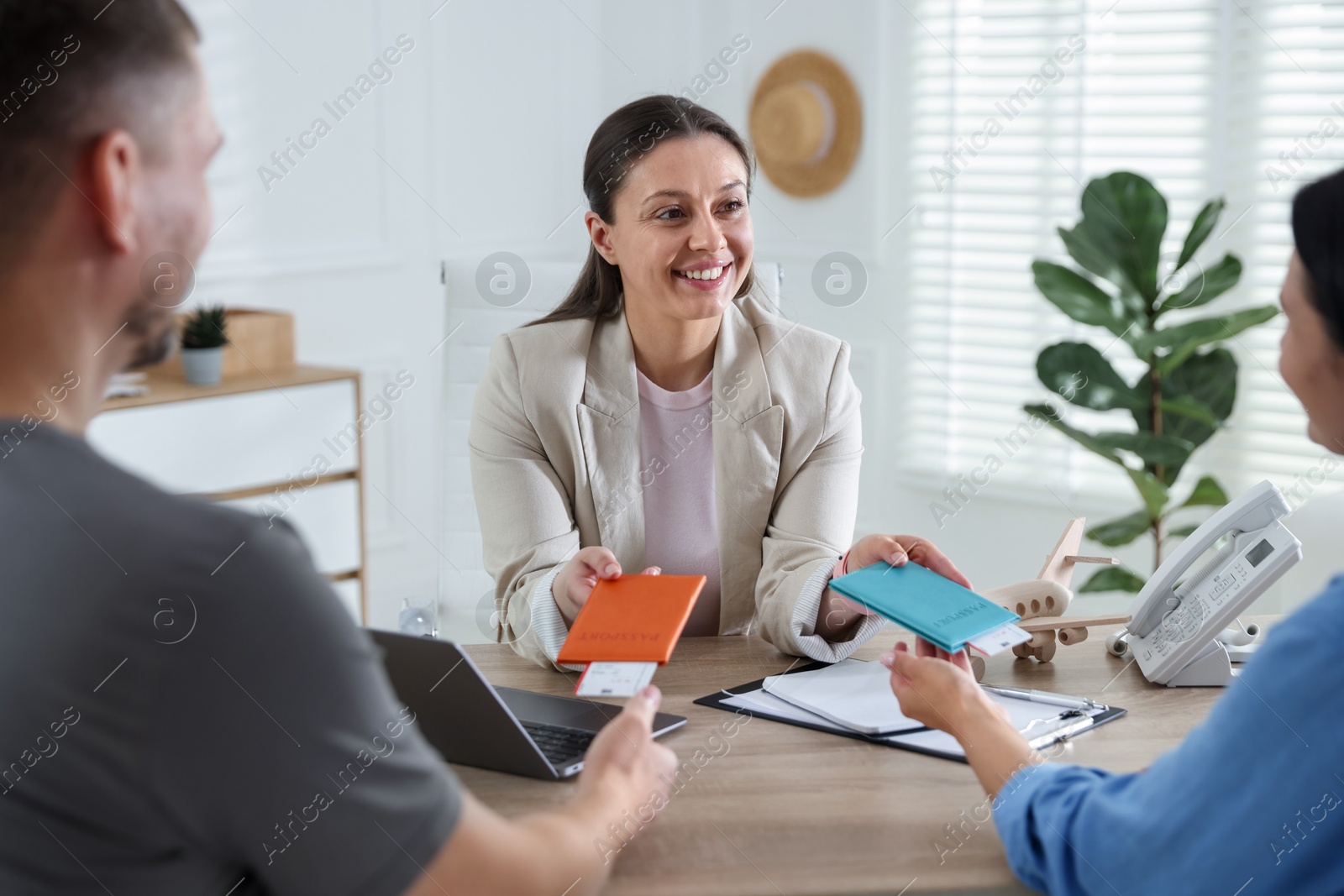 Happy couple planning vacation with travel agent at wooden table in office Photo of Happy couple planning vacation with travel agent at wooden table in office