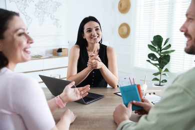 Photo of Happy couple planning vacation with travel agent at wooden table in office