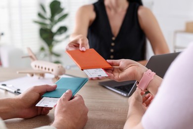 Photo of Travel agent giving passports with tickets to couple at wooden table in office, closeup
