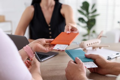 Photo of Travel agent giving passports with tickets to couple at wooden table in office, closeup