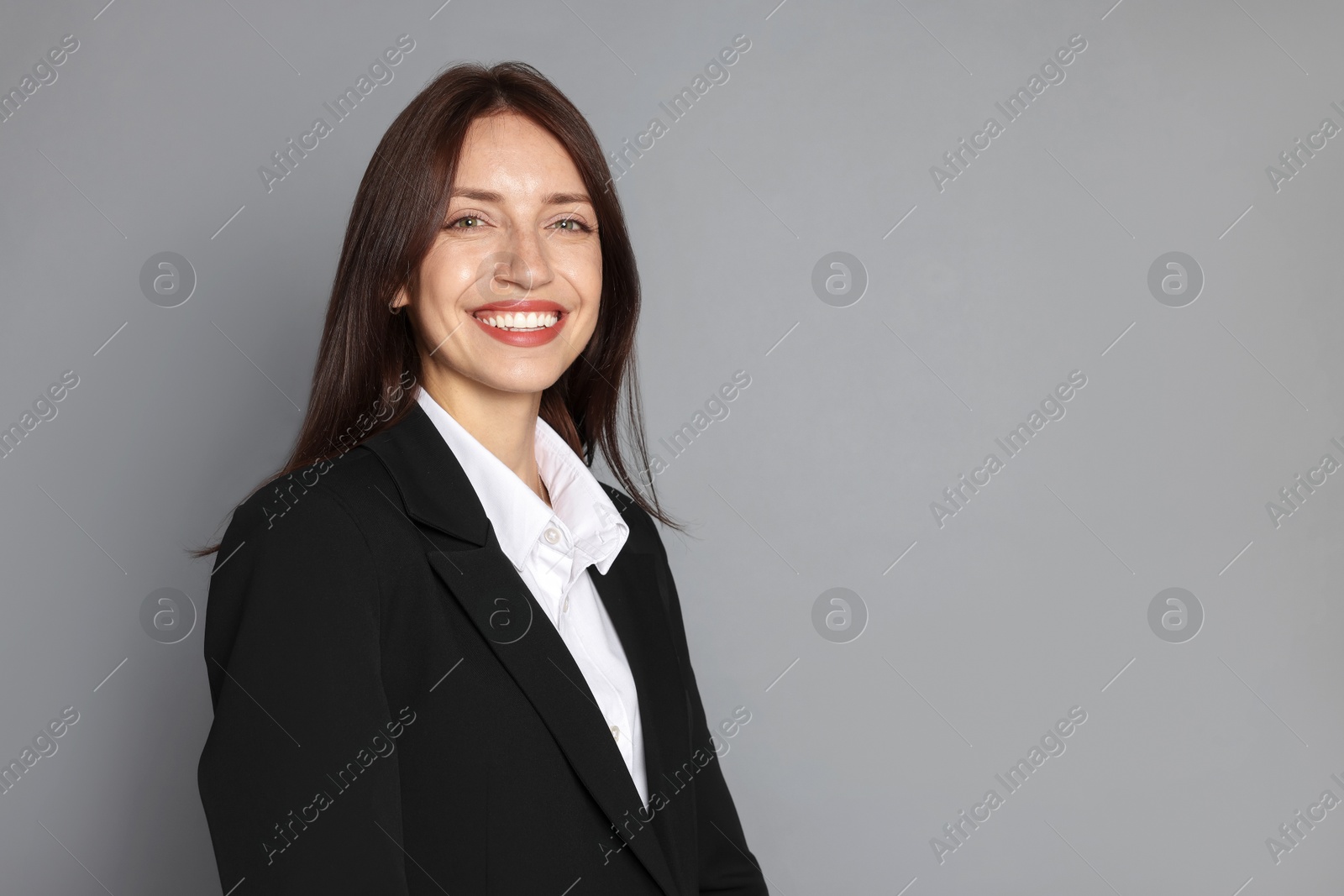 Happy woman in suit on grey background, space for text Photo of Happy woman in suit on grey background, space for text