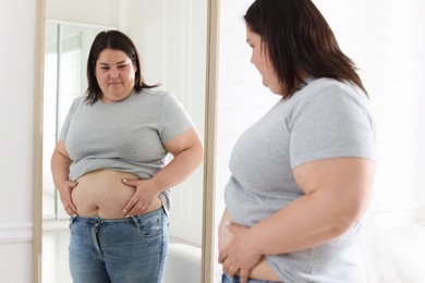 Photo of Woman with excessive belly fat near mirror indoors. Overweight problem