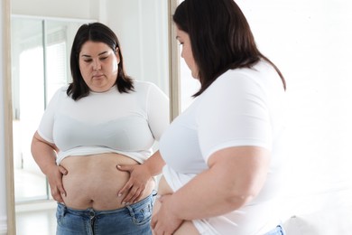 Photo of Woman with excessive belly fat near mirror indoors. Overweight problem
