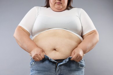 Photo of Overweight woman trying to put on tight jeans against grey background, closeup