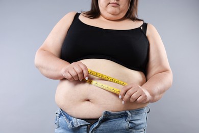 Photo of Overweight woman measuring her belly with tape on grey background, closeup