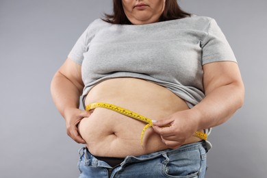 Photo of Overweight woman measuring her belly with tape on grey background, closeup