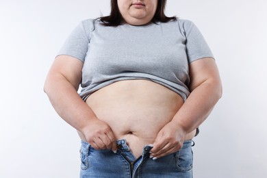Photo of Overweight woman trying to put on tight jeans against white background, closeup