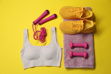 Photo of Sportswear, skipping rope, dumbbells, towel and sneakers on yellow background, flat lay