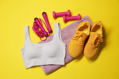 Photo of Sportswear, skipping rope, dumbbells, towel and sneakers on yellow background, flat lay