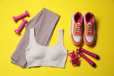 Photo of Sportswear, dumbbells, sneakers and skipping rope on yellow background, flat lay