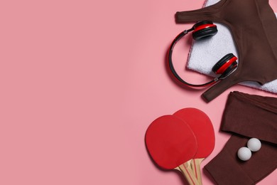 Photo of Sportswear, ping pong rackets, balls, towel and headphones on pink background, flat lay. Space for text