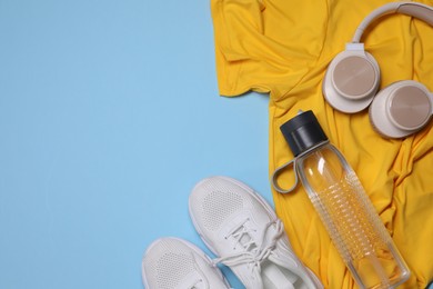 Photo of Sportswear, bottle of water, headphones and sneakers on light blue background, flat lay