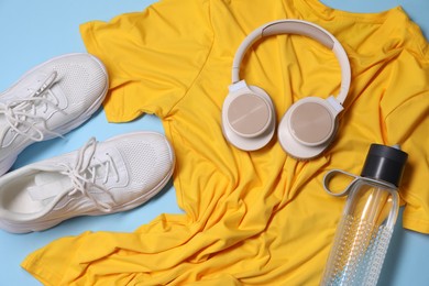 Photo of Sportswear, bottle of water, headphones and sneakers on light blue background, flat lay