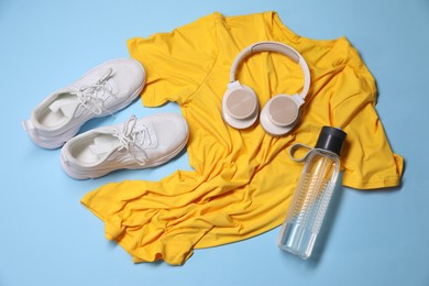 Photo of Sportswear, bottle of water, headphones and sneakers on light blue background, flat lay