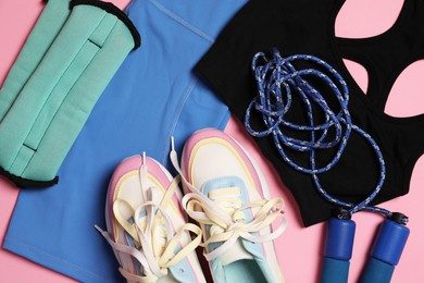 Photo of Sportswear, ankle weights, skipping rope and sneakers on pink background, flat lay